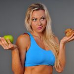 A sporty fit woman in her fitness clothes holding an apple and blueberry muffin