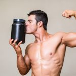 Shirtless muscular man kissing nutritional supplement over white background